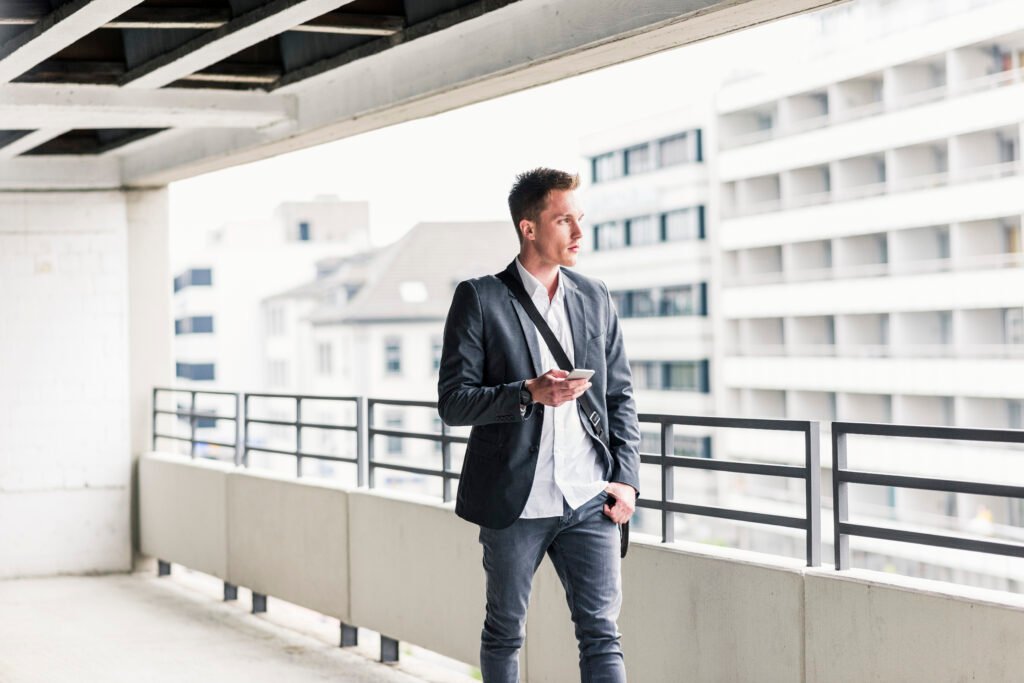 Young businessman using smartphone, walking on parking level